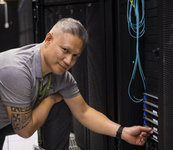 Man kneeling and looking at the camera while touching the Data centre cable server