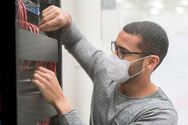 IT technician wearing a facemask while fixing a server at the office